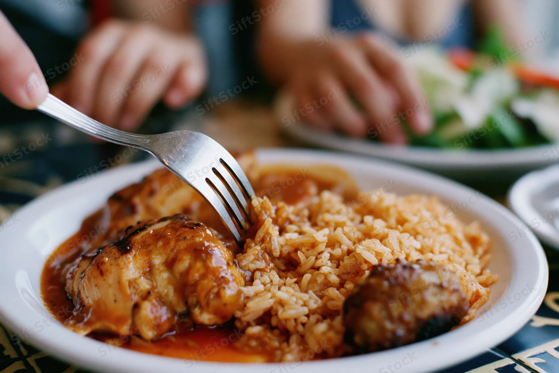Fork pressing into grilled chicken and rice on a plate at a dining table