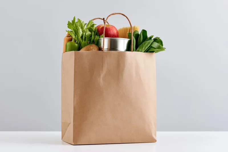 Kraft paper grocery bag filled with fresh vegetables and fruit on a white surface