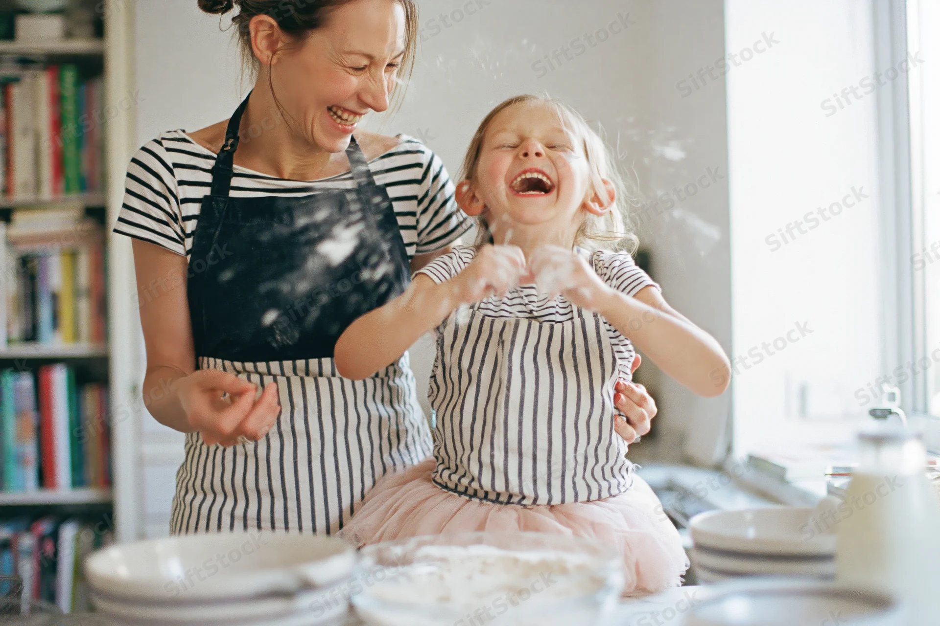 Woman and young girl laughing while baking together in a kitchen