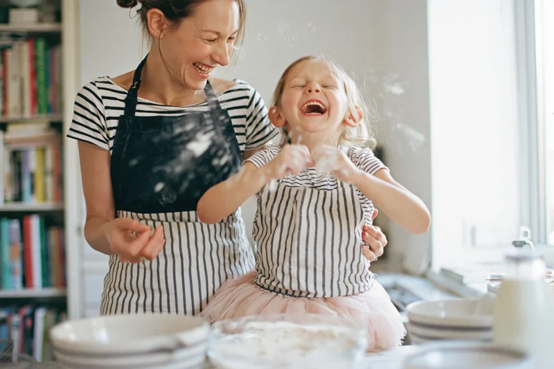 Woman and young girl laughing while baking together in a kitchen