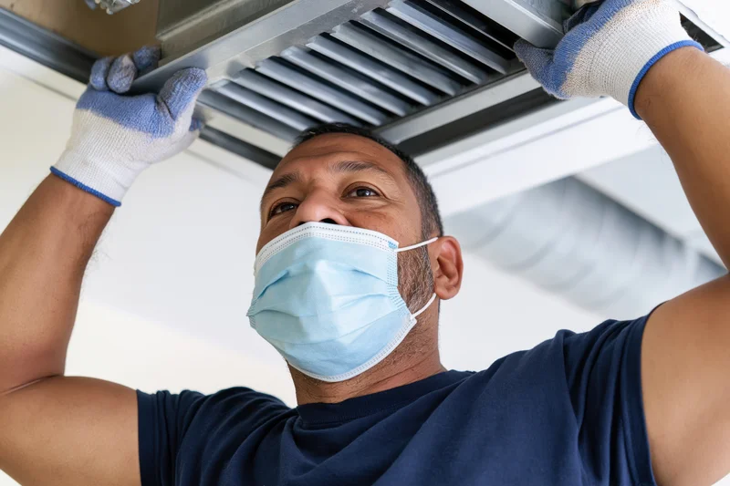 Man installing air conditioning duct on ceiling indoors