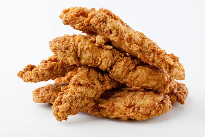 Crispy fried chicken tenders stacked loosely on white background