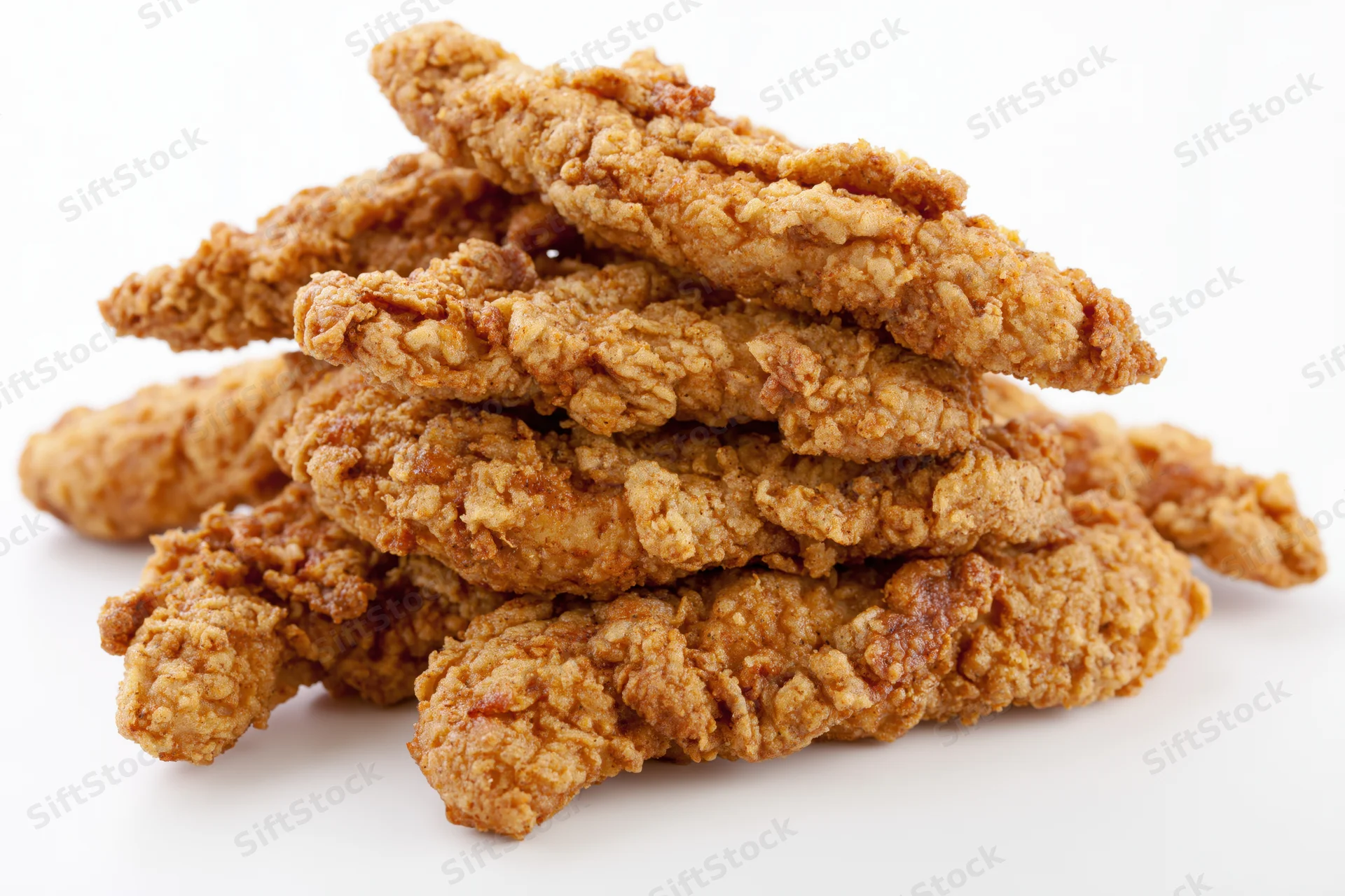Crispy fried chicken tenders stacked loosely on white background
