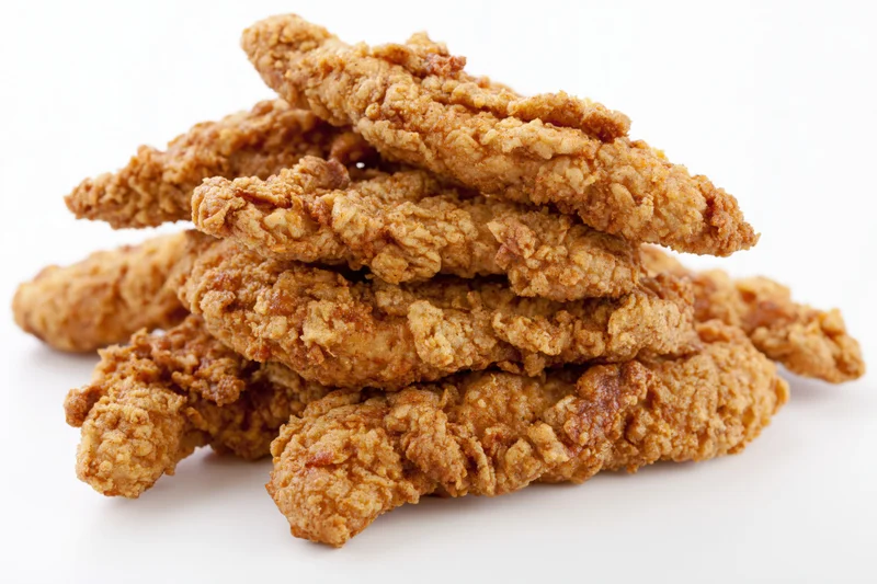 Crispy fried chicken tenders stacked loosely on white background