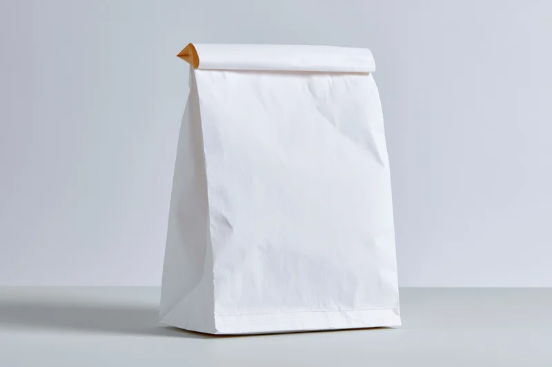 White paper bag standing upright on flat surface with blank front for branding