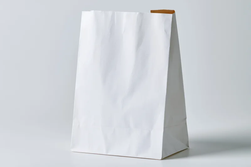 White paper bag standing upright on flat surface with blank front for branding