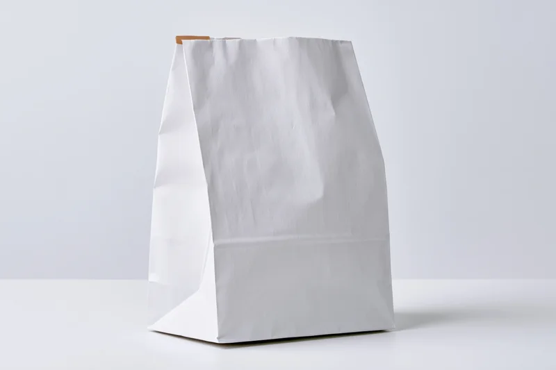 White paper bag standing upright on a flat surface with copyspace for branding or design