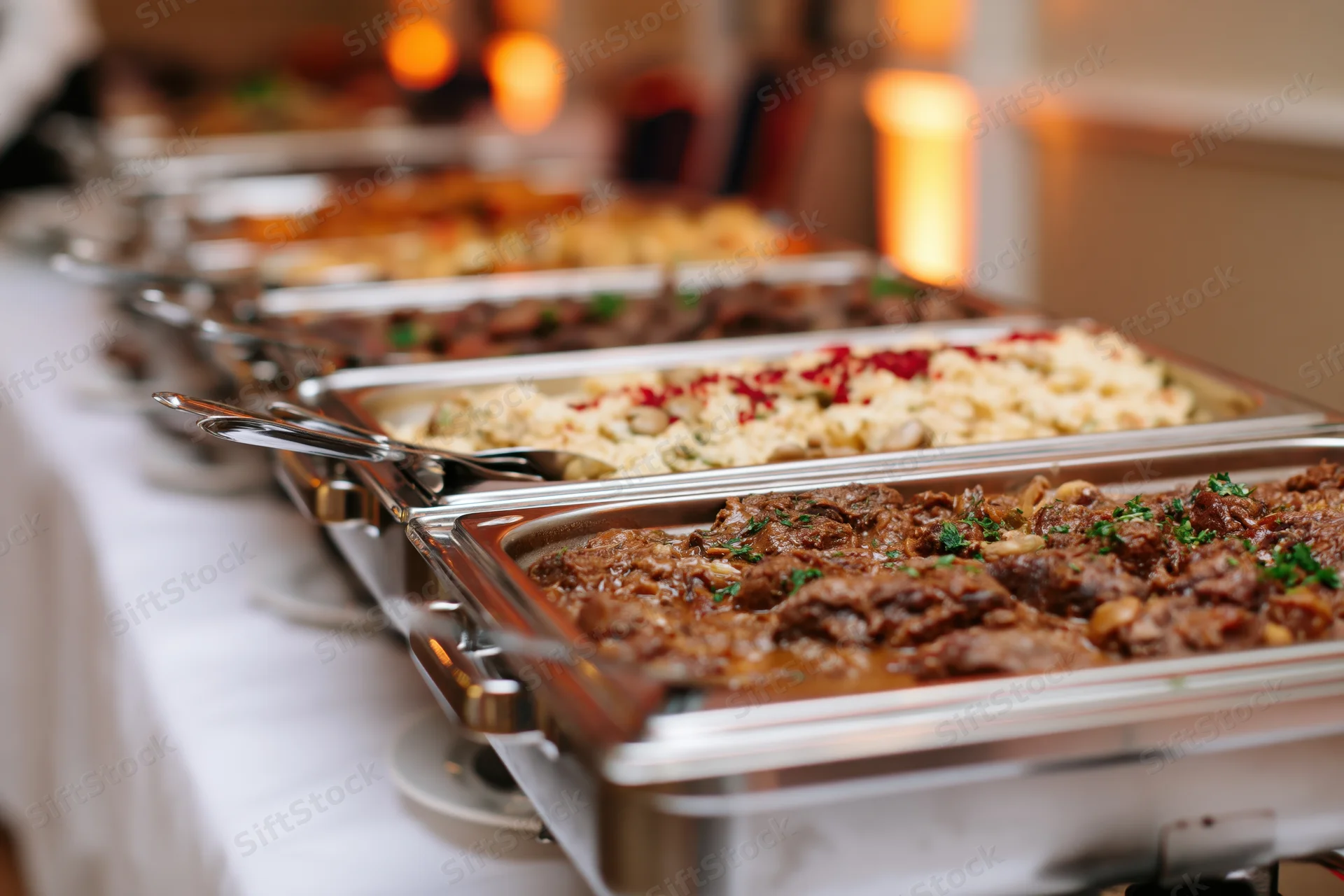 Row of stainless steel chafing dishes filled with hot food on a buffet table at an event