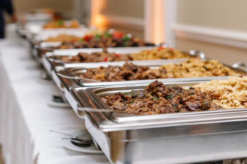 Row of stainless steel chafing dishes filled with hot food on a buffet table at an event
