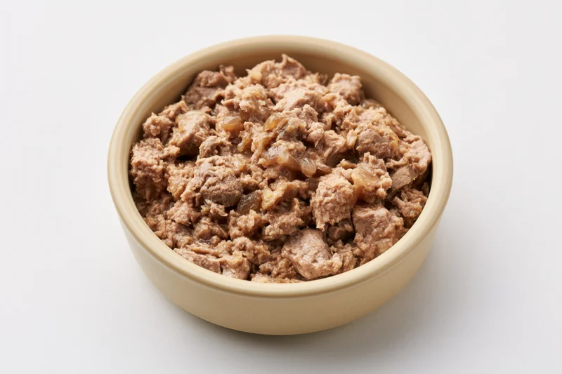 Chunky wet cat food in a small beige ceramic bowl on white background
