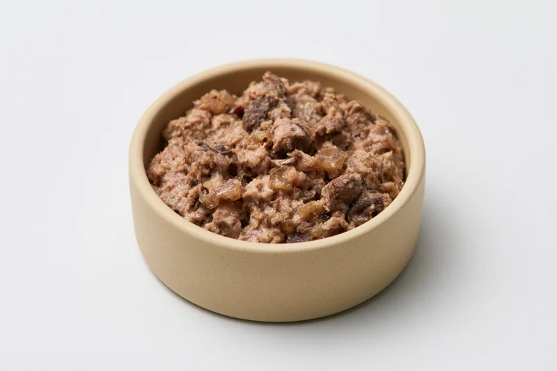 Chunky wet cat food in a small beige ceramic bowl on white background