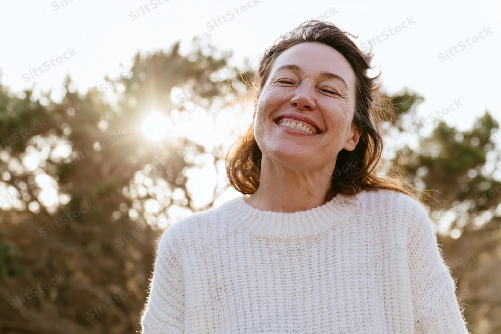 Woman smiling with head tilted back in sunlight outdoors