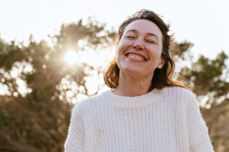 Woman smiling with head tilted back in sunlight outdoors