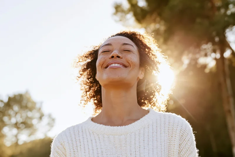 Woman smiling with head tilted back in sunlight outdoors