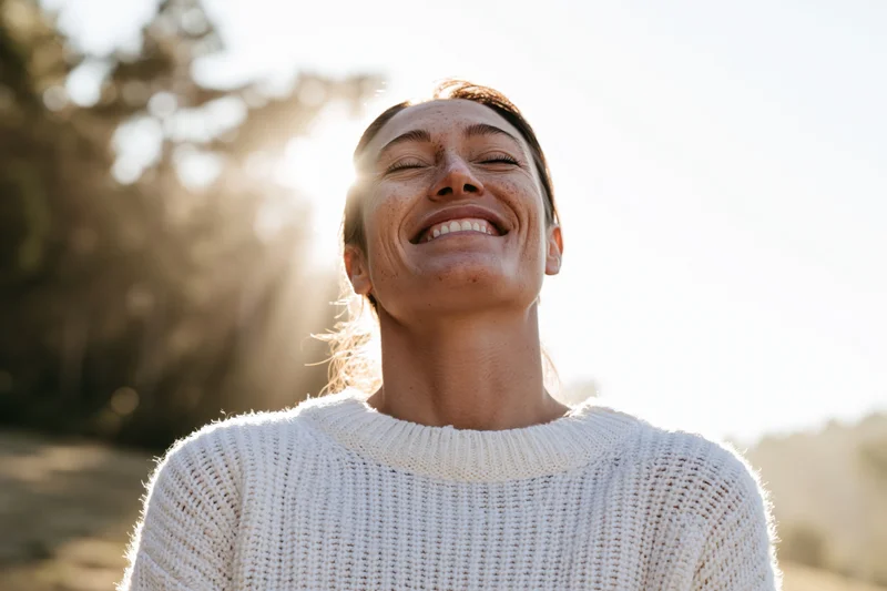 Woman smiling with head tilted back in sunlight outdoors