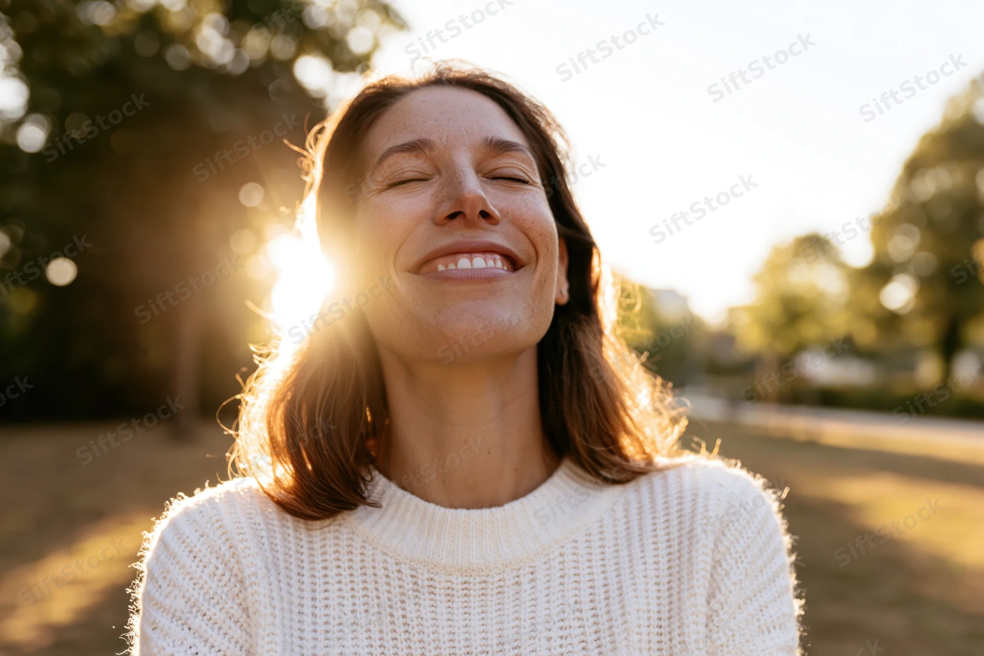 Woman smiling with eyes closed in sunlight at park