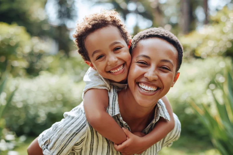 Woman carrying child on her back smiling in a lush garden