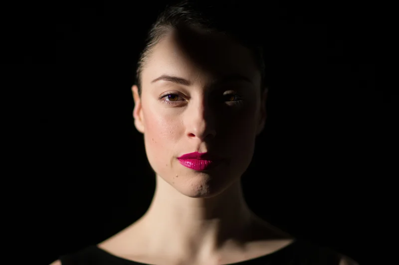 Young woman with dark hair pulled back in a studio portrait with dramatic lighting and pink lipstick