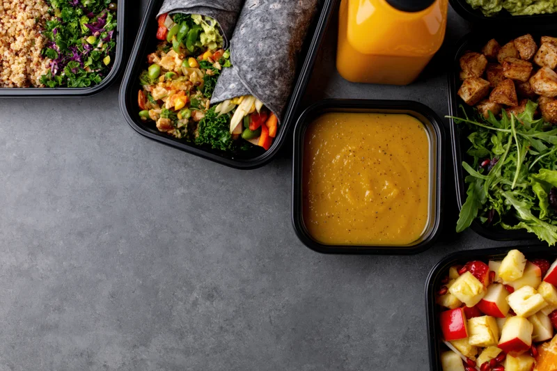 Assorted healthy meal prep containers arranged along the right side of a gray countertop with copyspace on the left