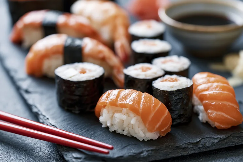 Assorted sushi nigiri and rolls with chopsticks on dark slate plate