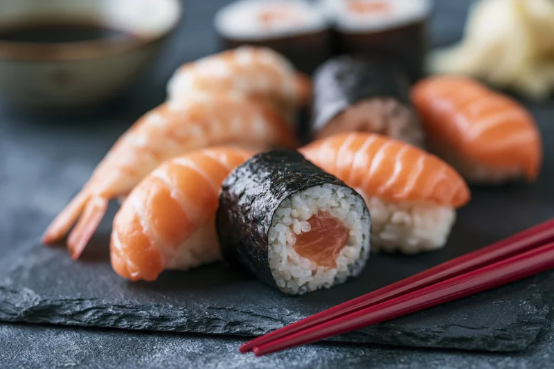 Assorted sushi nigiri and rolls with chopsticks on dark slate serving plate