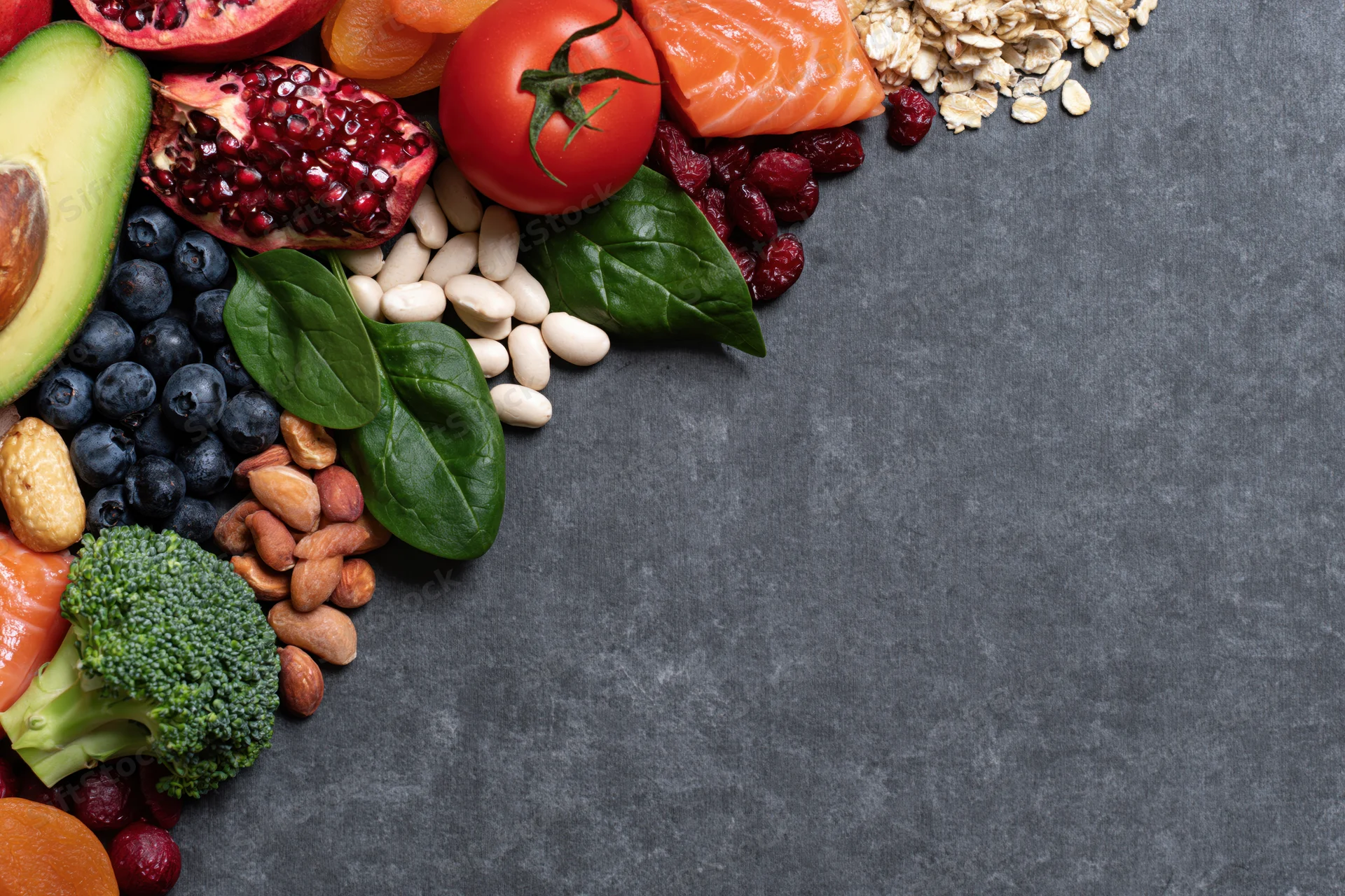 Healthy whole foods arranged along the right edge on dark surface with copyspace