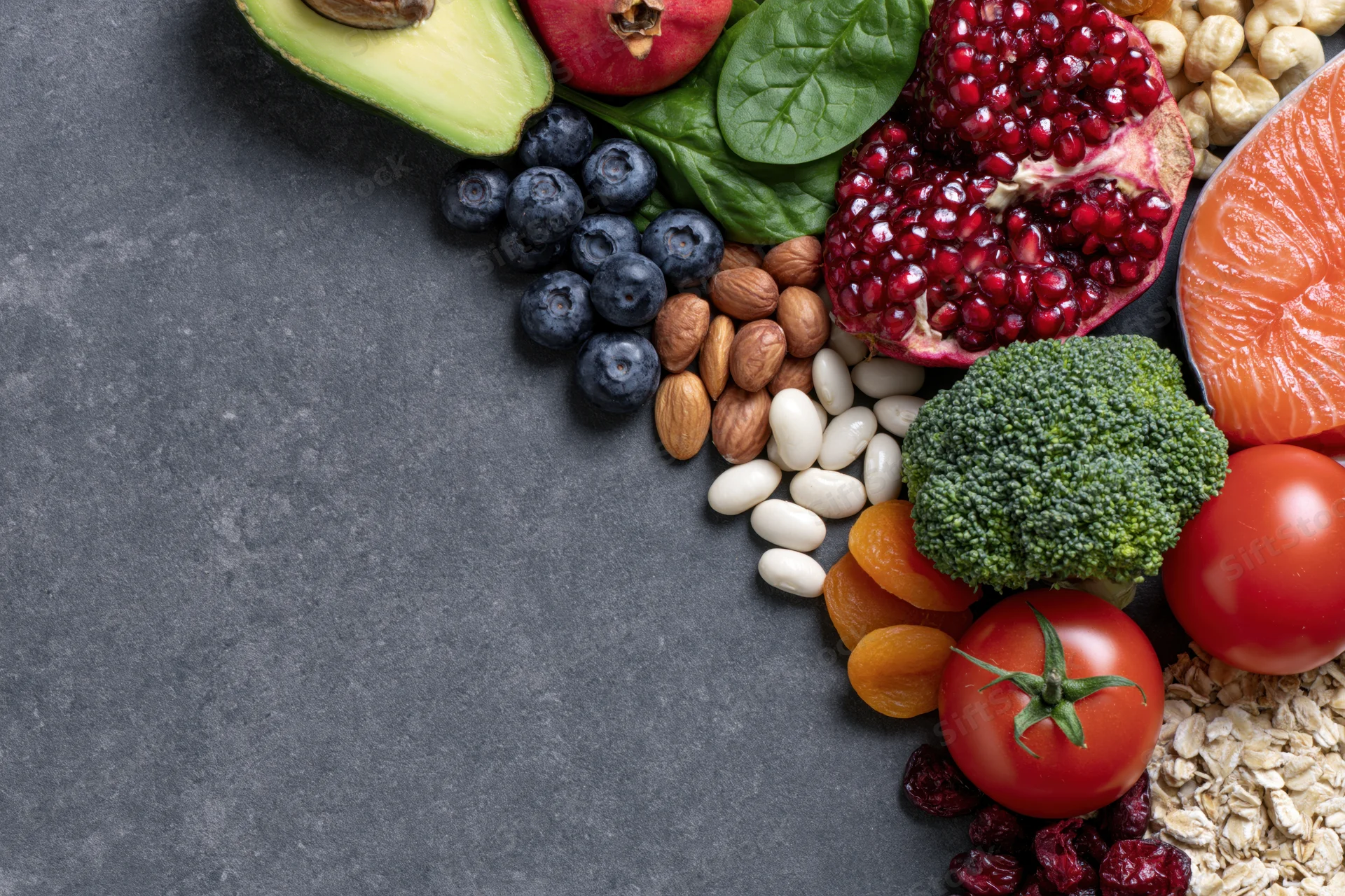 Healthy whole foods arranged along the right edge on dark surface with copyspace