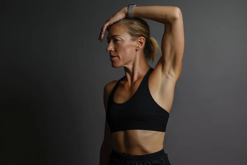 Athletic woman stretching arm overhead across forehead in studio setting