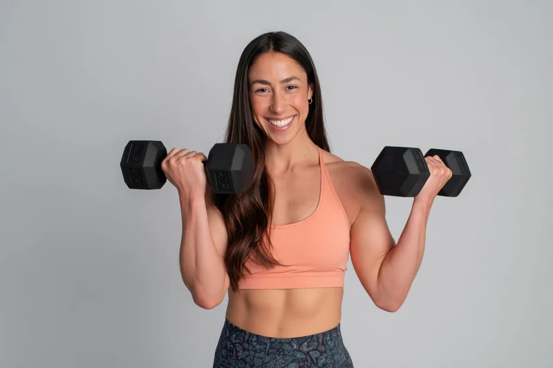 Smiling athletic woman lifting dumbbells in studio wearing sportswear