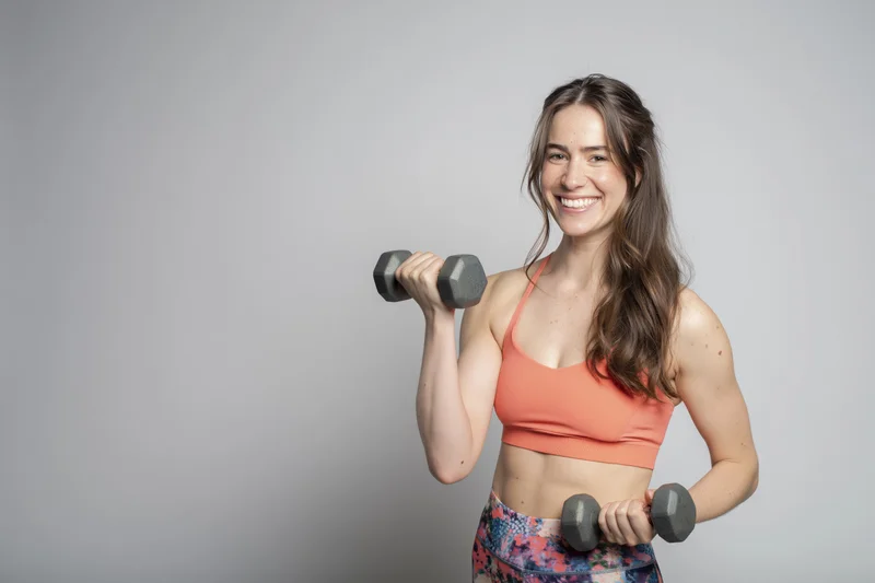 Woman lifting dumbbells while smiling in a studio setting