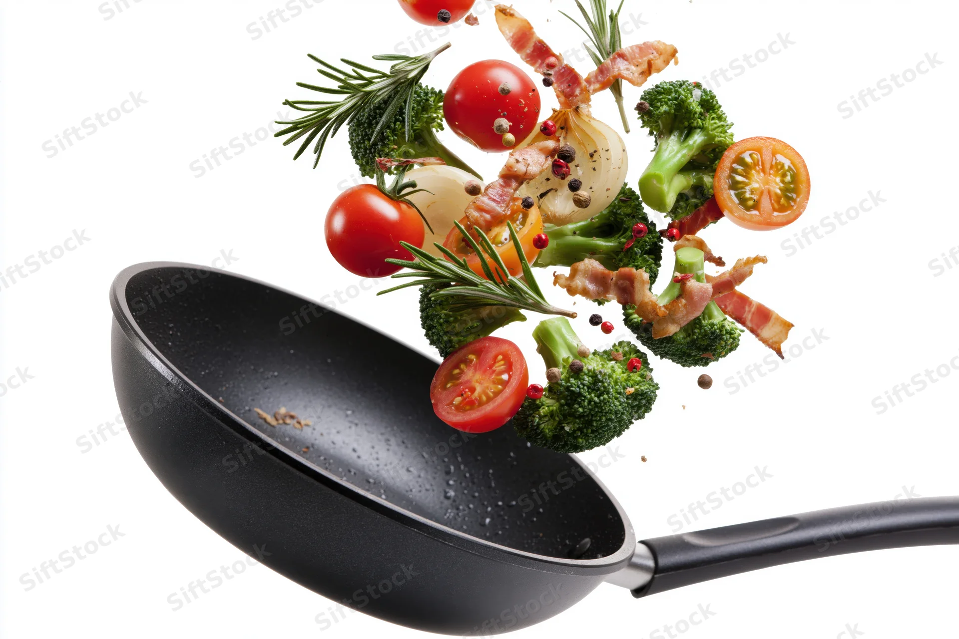 Black nonstick frying pan tilted mid-toss with vegetables and bacon flying out against white background