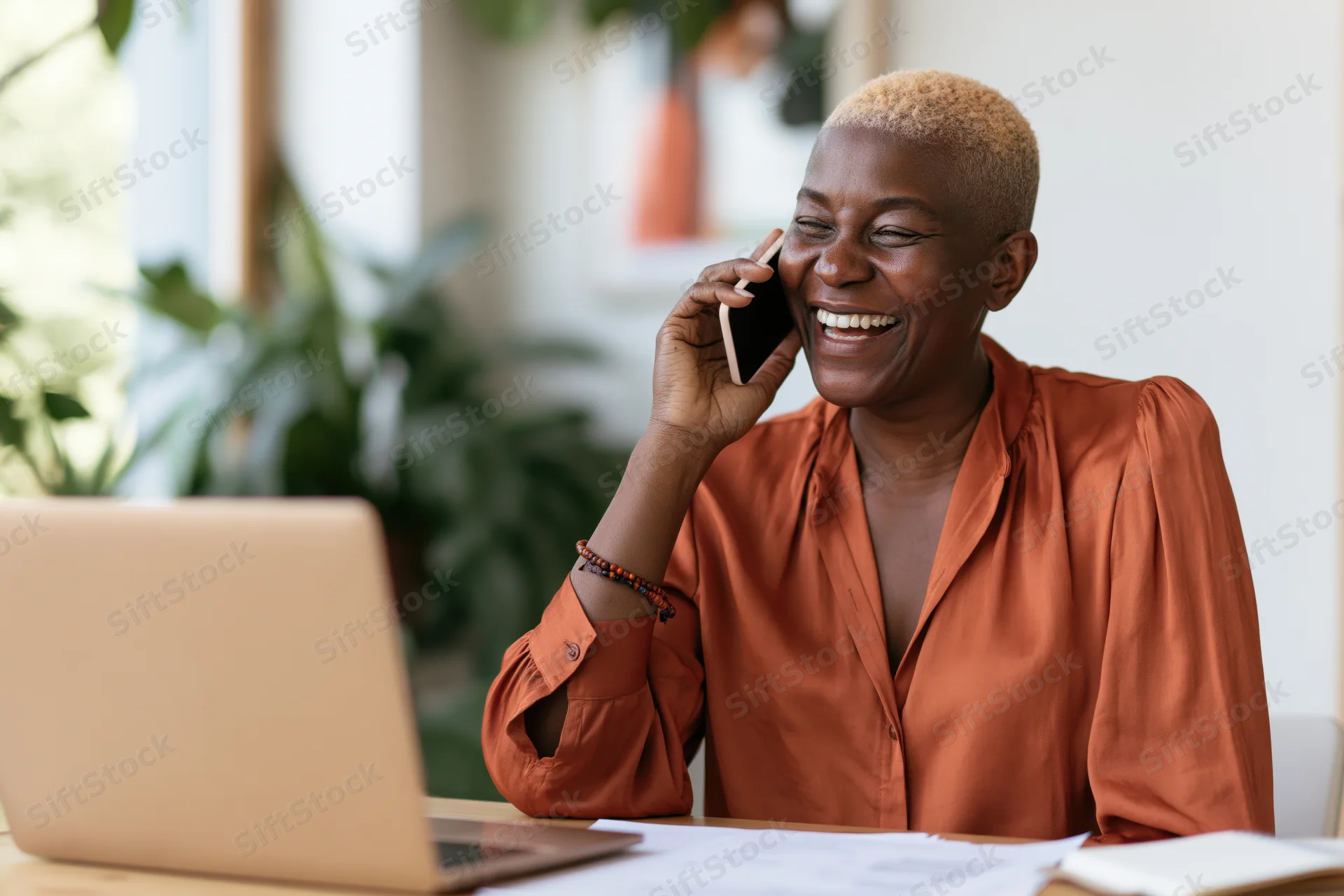 Woman laughing while talking on phone at desk with laptop in office setting