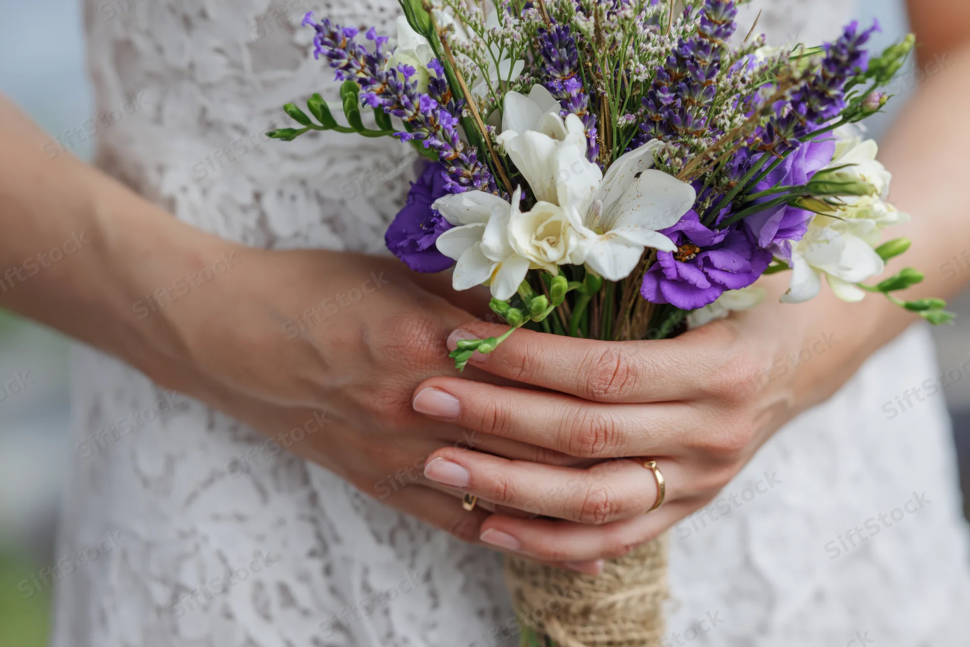 Bride holding rustic wedding bouquet of lavender and white flowers in lace dress