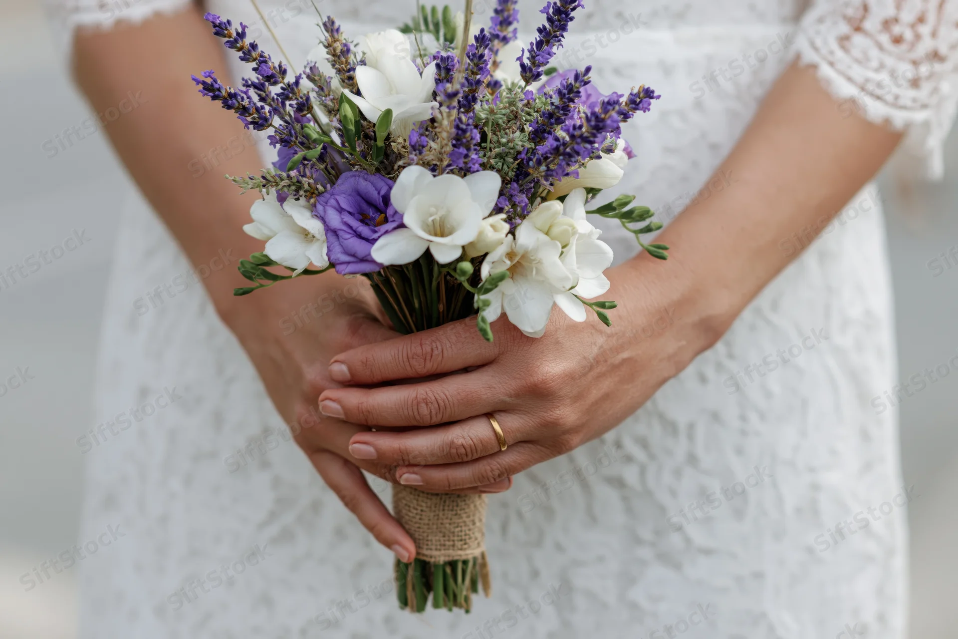 Bride holding rustic floral bouquet with lavender and white flowers in lace dress