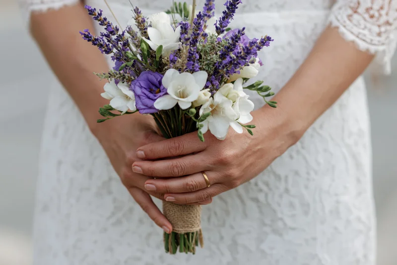 Bride holding rustic floral bouquet with lavender and white flowers in lace dress