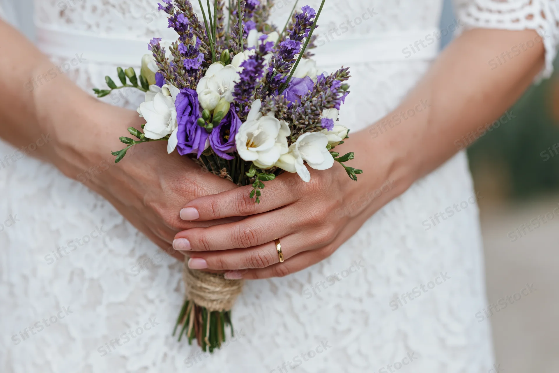 Bride holding rustic wedding bouquet of lavender and white flowers in lace dress