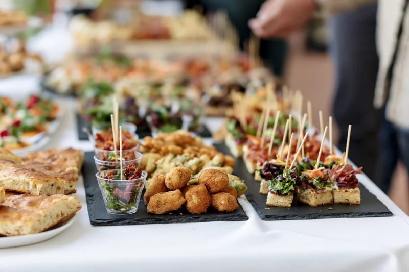 Assorted finger foods arranged on a buffet table with slate trays and glass cups for a party event