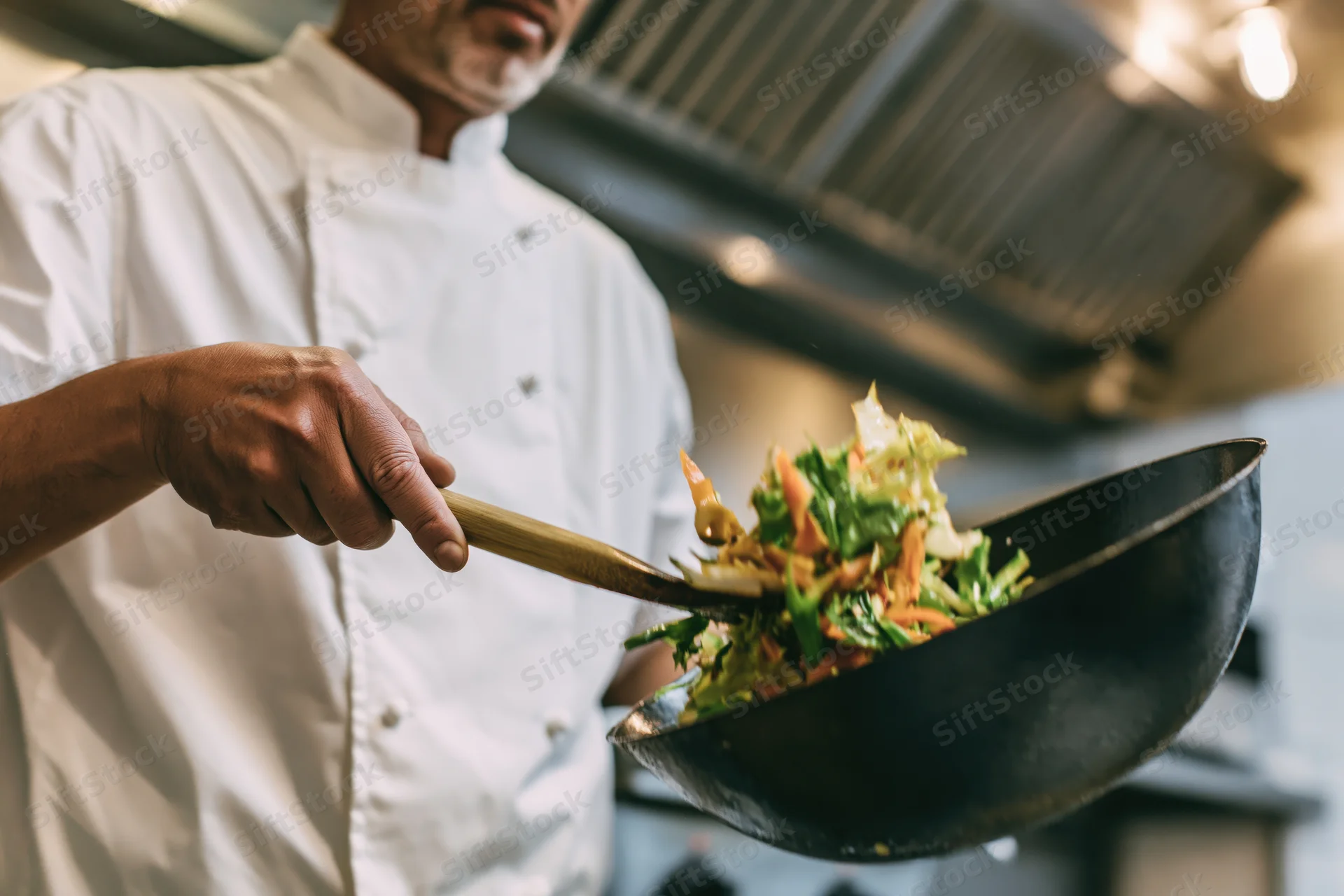 Chef tossing vegetables in a wok in a commercial kitchen