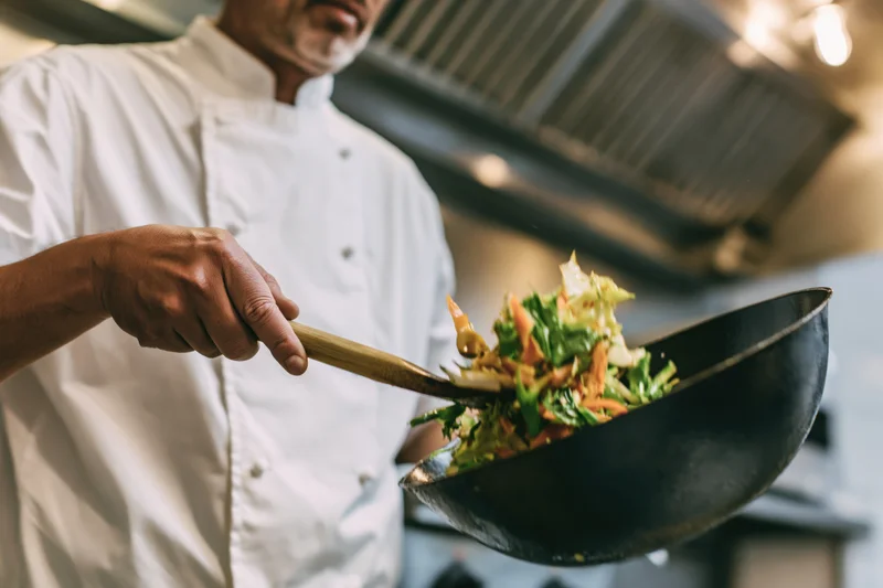 Chef tossing vegetables in a wok in a commercial kitchen