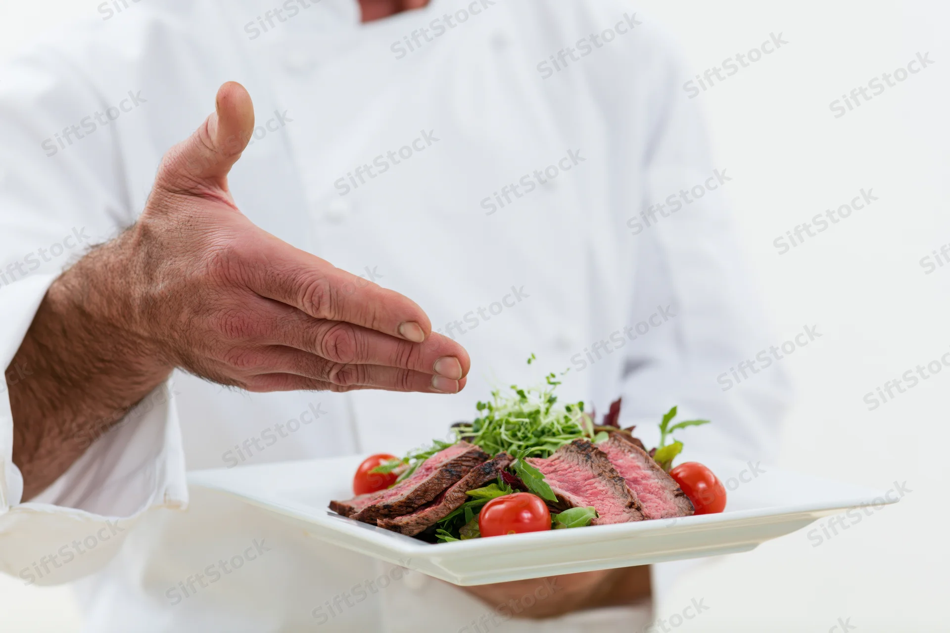 Chef presenting a plated steak salad with tomatoes and greens on a white plate