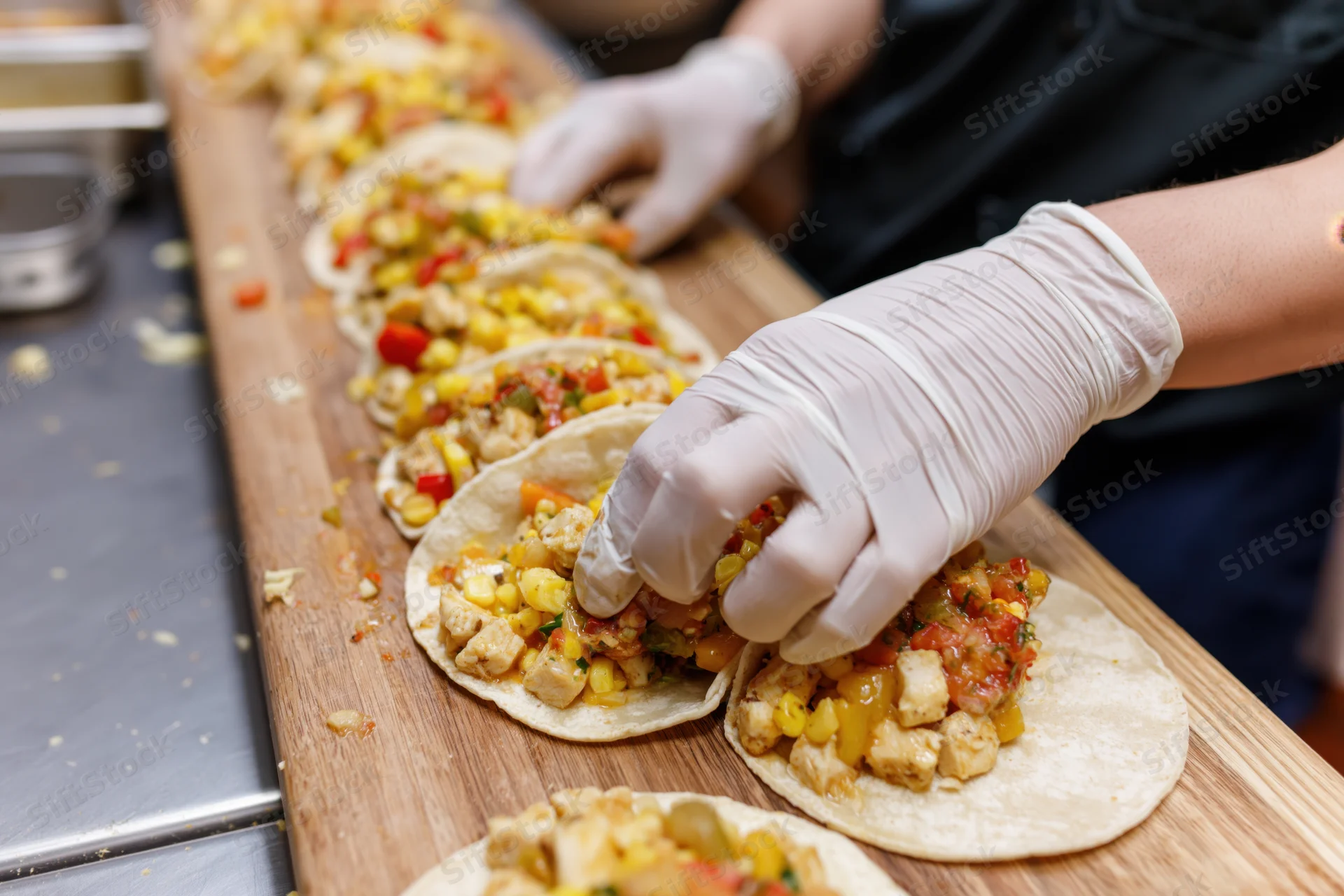 Chef assembling open-faced tacos in a row on a wooden board in a kitchen