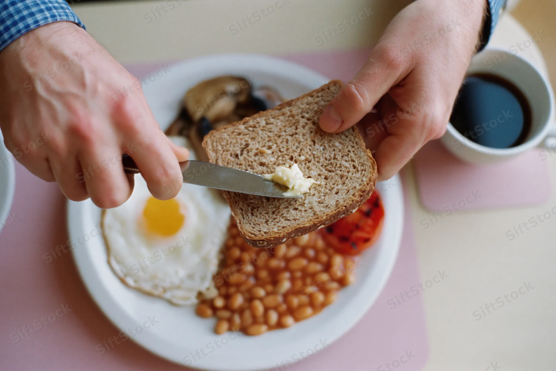 Man buttering wholemeal toast with knife over plate of breakfast food on table