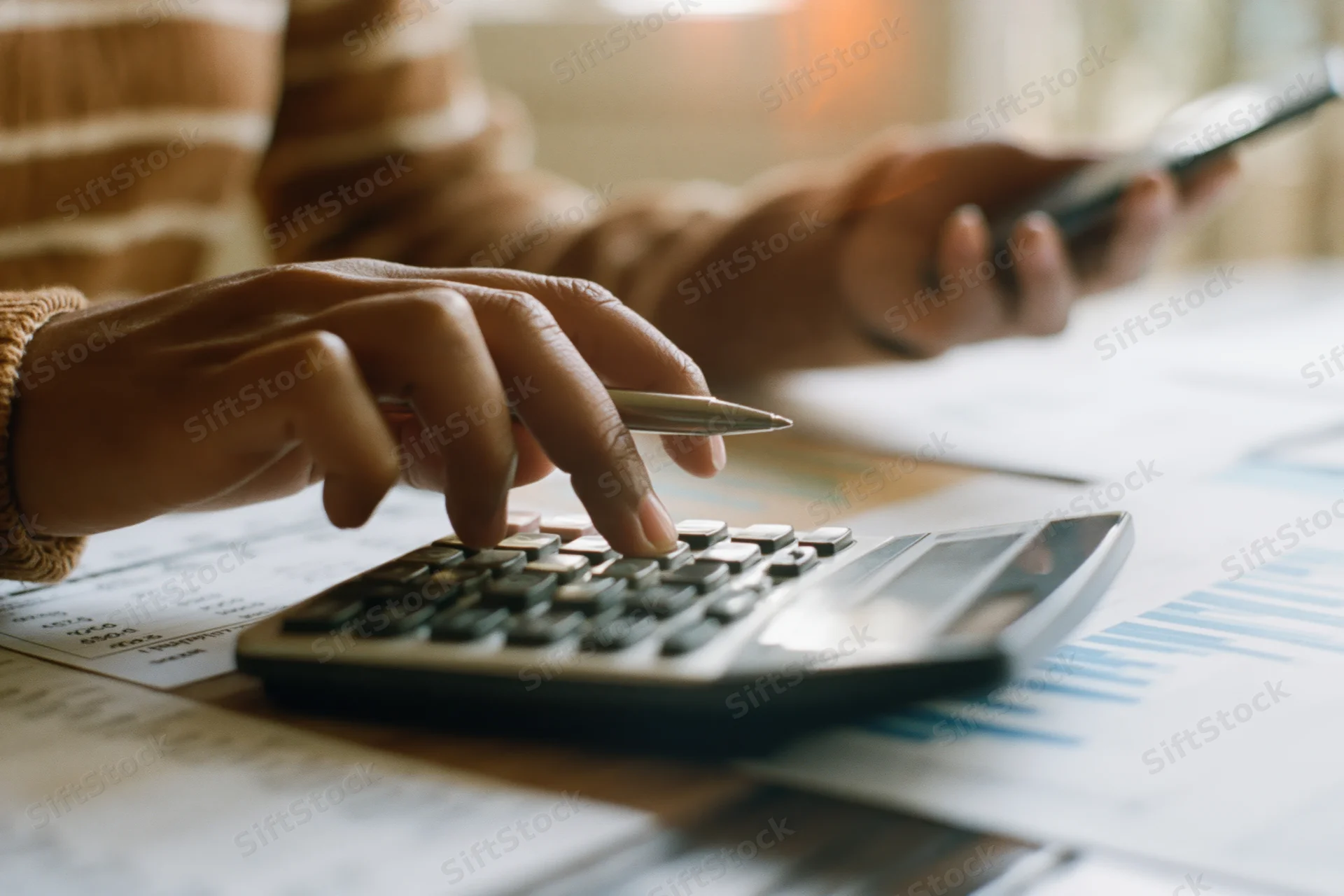 Woman's hands using calculator and pen over financial documents on desk