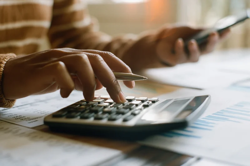 Woman's hands using calculator and pen over financial documents on desk
