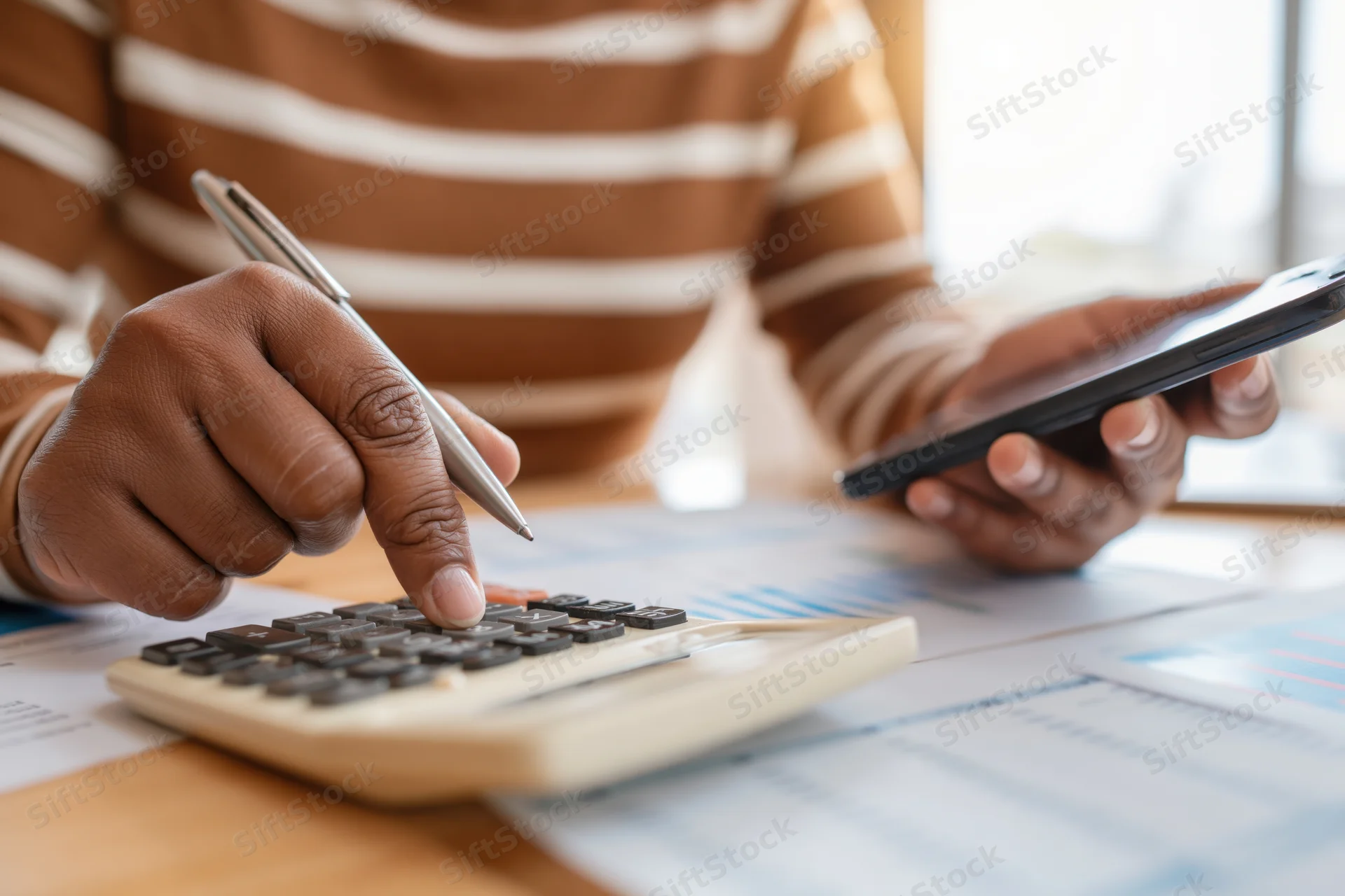Woman’s hands using calculator and smartphone over financial documents on desk
