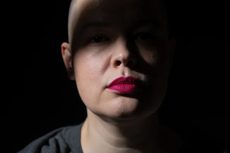 Close-up portrait of a young woman with shaved head and red lips in dramatic studio lighting