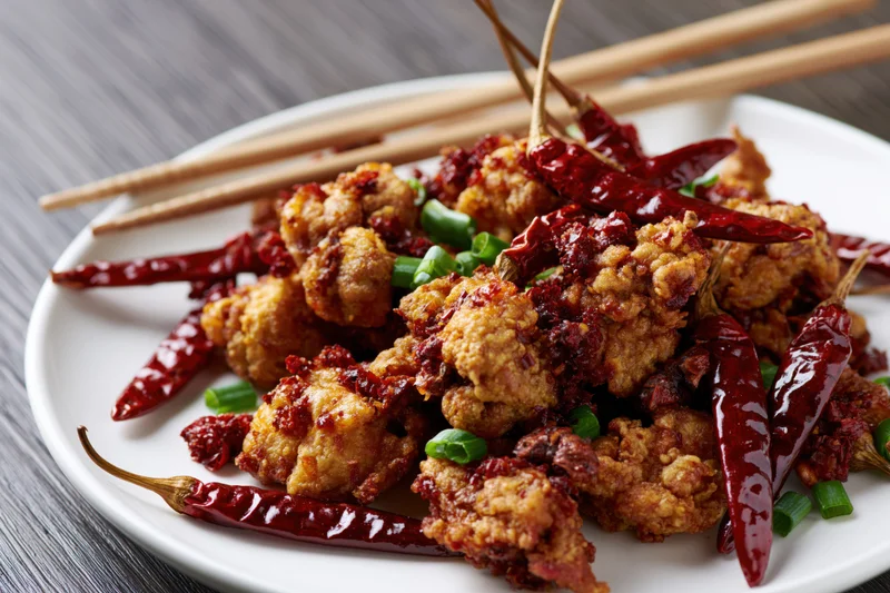 Crispy fried chicken pieces with dried red chilies and green onions on a white plate with chopsticks