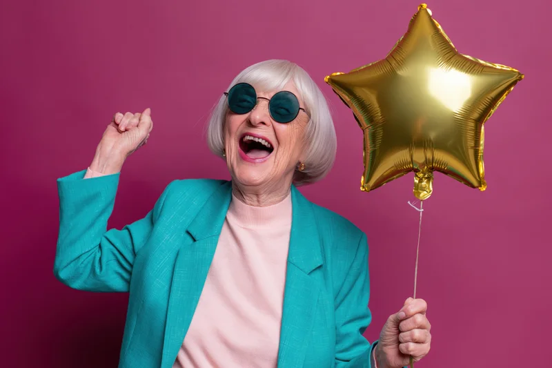 Elderly woman laughing with gold star balloon in studio setting