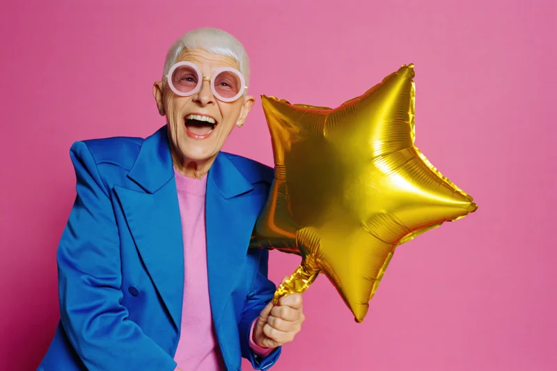 Senior woman laughing while holding a gold star balloon against pink background