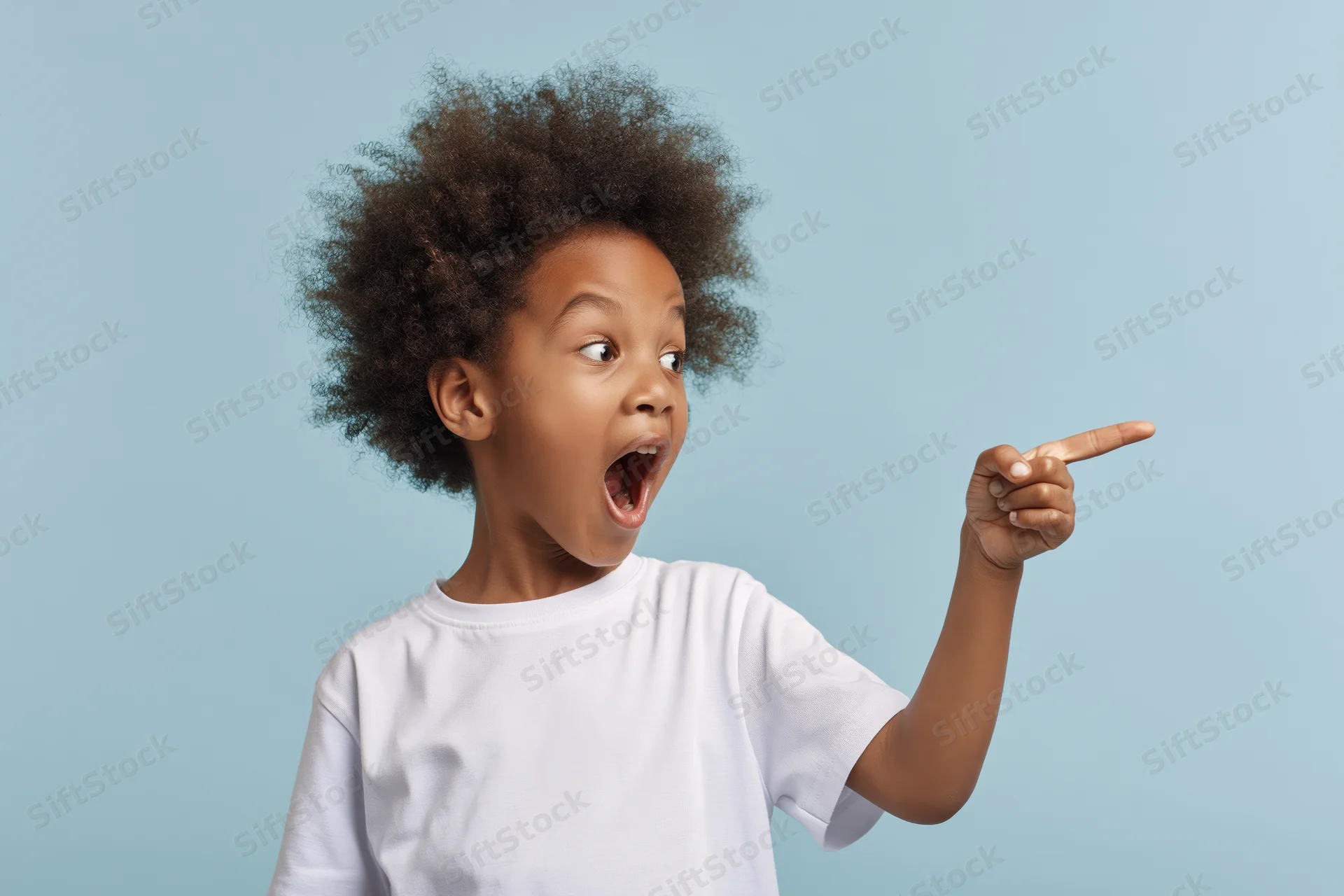 Excited young black boy pointing to the side with open mouth in studio portrait